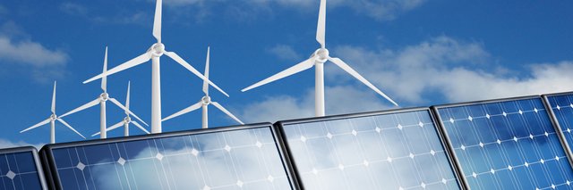 Windkraftanlagen hinter einer Reihe von Solarmodulen vor blauem Himmel